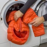 Eine Person steckt eine wattierte Jacke in eine Waschmaschine.