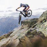 Mann springt mit E-Mountainbike über ein Hindernis in den Bergen.