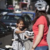 Eine Frau reicht einem Mädchen neben einem Fahrrad einen Helm.