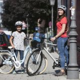 Ein Mädchen und eine Frau stehen mit Fahrrädern auf einem Bürgersteig. Beide tragen Helm.