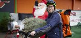Ein Mann steht mit einem E-Bike vor einer Verkaufsstelle für Weihnachtsbäume. Einen verpackten Weihnachtsbaum hat er auf Lenker und Sattel abgelegt.