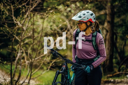 Frau mit Helm schiebt Mountainbike durch Wald