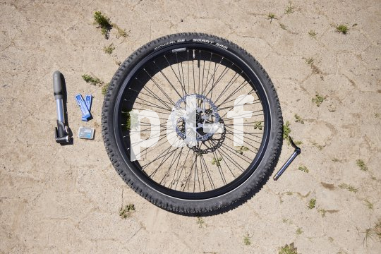 Das Vorderrad eines Fahrrades liegt auf dem Boden, daneben eine Luftpumpe, Reifenheber und eine kleine Box mit Flickzeug.