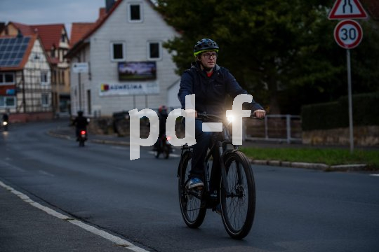 Ein Mann fährt in der Dämmerung mit dem Fahrrad auf einer Straße. Sehr deutlich zu sehen ist der leuchtende Frontscheinwerfer.