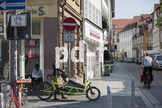 Eine Frau steht neben einem Lastenrad am Eingang einer innerstädtischen Einbahnstraße und zeigt auf das Verkehrsschild dazu. Ihr Fahrradhelm hängt am Lenker.