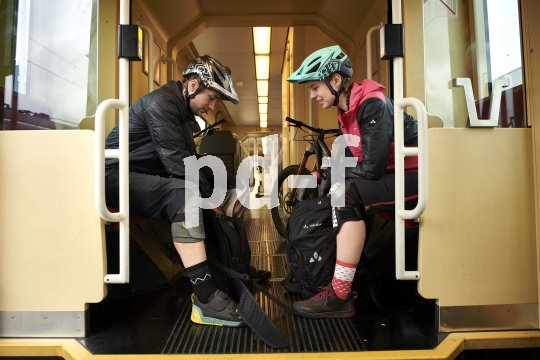 Ein Mann und eine Frau mit Fahrradhelmen sitzen sich im Zug gegenüber. Im Hintergrund ist ein Mountainbike zu erkennen.
