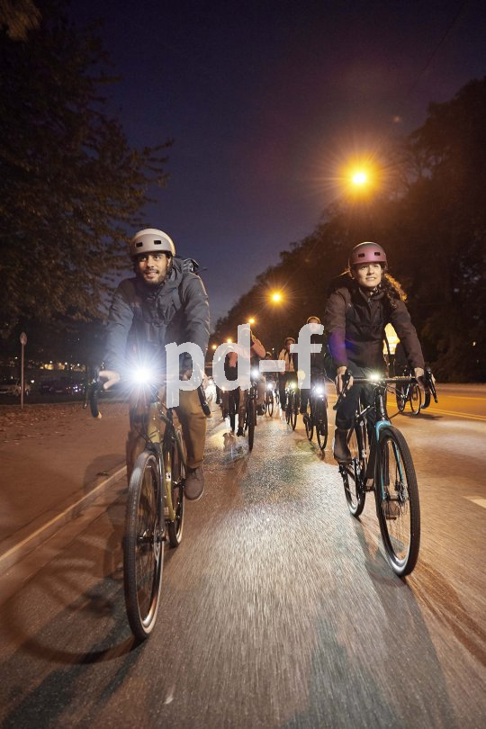 Eine Gruppe Radfahrer:innen mit deutlich sichtbarer Beleuchtung fährt bei Dunkelheit auf einer Straße auf die Kamera zu.