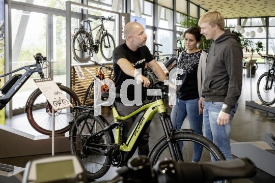 Ein Mann steht mit einem E-Bike in einem Fahrradladen und unterhält sich mit einer Frau und einem Mann.