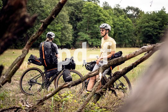 Zwei Personen stehen mit Fahrrädern mit Bikepacking-Taschen daran am Waldrand.
