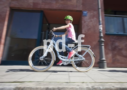 Ein Kind fährt mit einem Fahrrad auf einem Fußweg vor einem Gebäude.