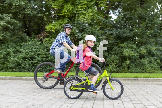 Ein Mann und ein Kind fahren auf Fahrrädern einen gepflasterten Weg entlang.