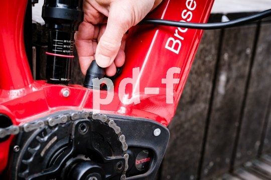 Eine Person schließt ein Ladekabel am Rahmen eines E-Bikes an.