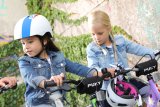 Zwei Mädchen stehen mit Fahrrädern herum, eine mit Helm auf den Kopf und eine mit dem Helm am Lenker hängend.