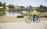 Mann fährt mit Fahrrad vor See und Brücke