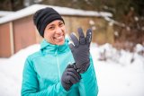 Eine lachende Frau zieht sich in verschneiter Umgebung Handschuhe an.