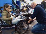 Die Sportlerin Kristina Vogel sitzt auf einem Trike mit Handkurbeln, das von einem Mitarbeiter des Herstellers HP Velotechnik angepasst wird.