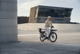 Eine Person auf einem E-Bike mit längerem Gepäckträger vor moderner Architektur.