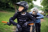 Ein Junge mit Fullface-Helm lehnt auf dem Lenker eines Mountainbikes und schaut sich um.