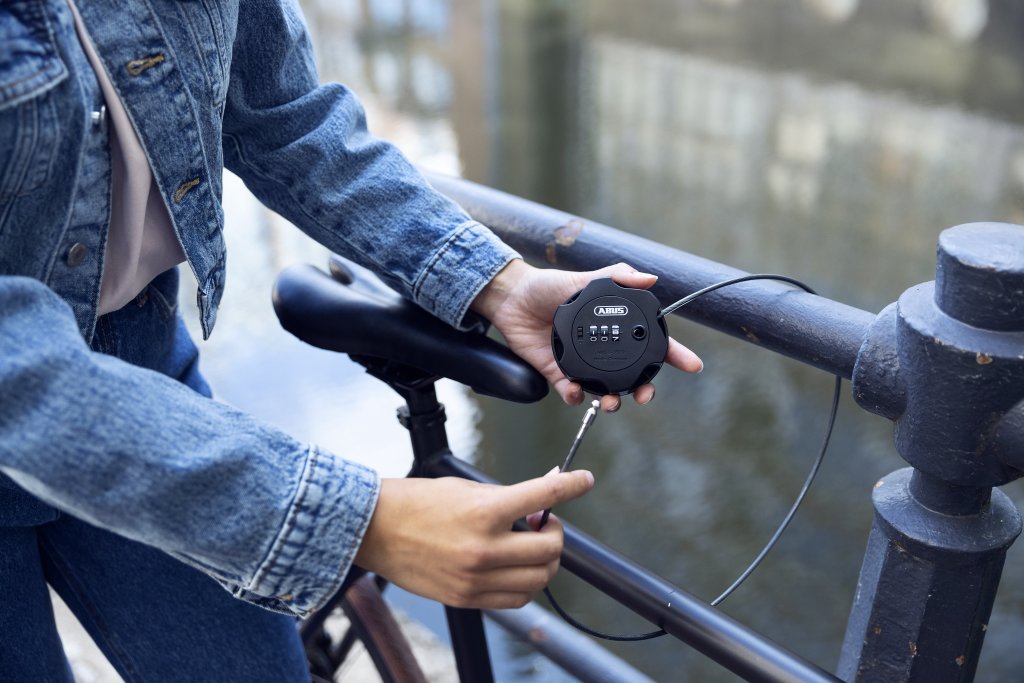 Eine Person schließt ein Fahrrad mit einem dünnen Stahlseil an einem Geländer an.