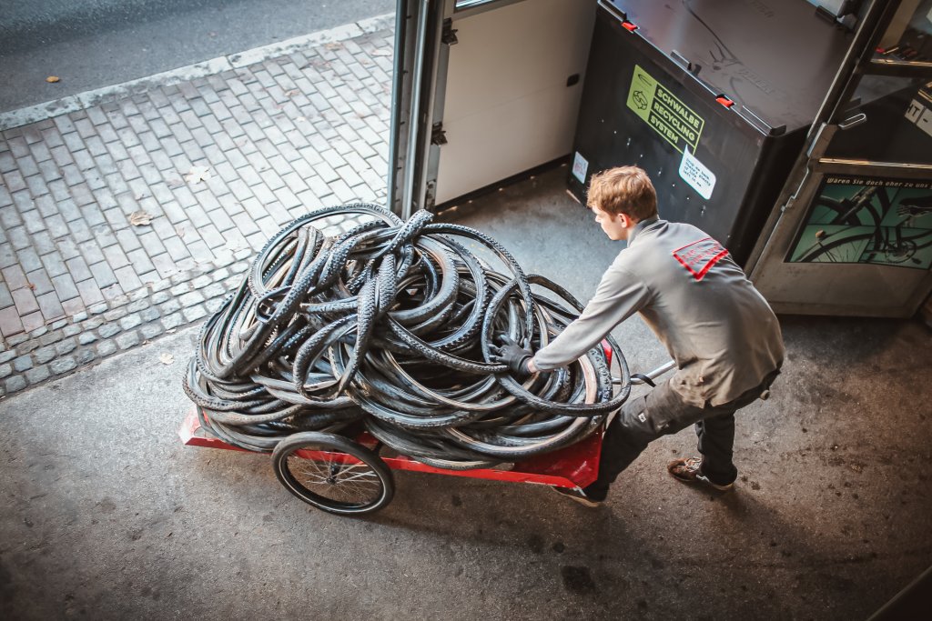 Ein Mann schiebt einen Fahrradanhänger mit alten Fahrradreifen aus einem Tor heraus.
