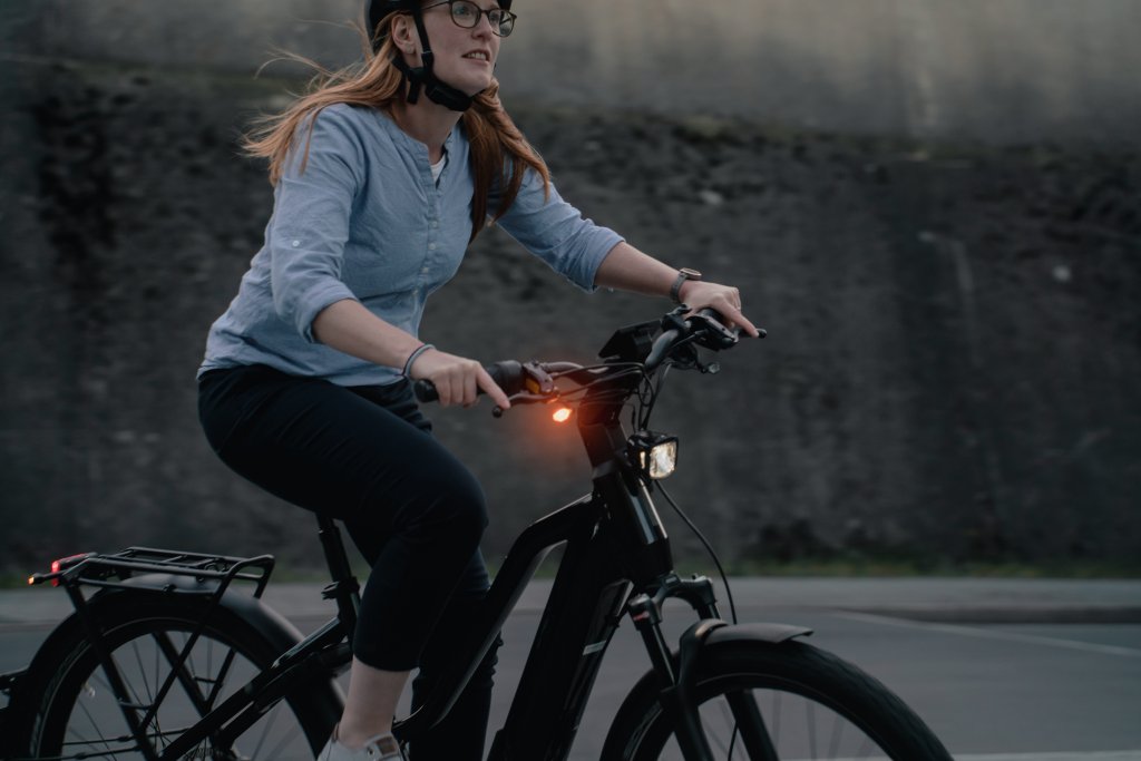 Eine Frau fährt in der Dämmerung ein E-Bike. An der rechten Seite des Lenkers ist ein orangefarbenes Licht zu sehen.