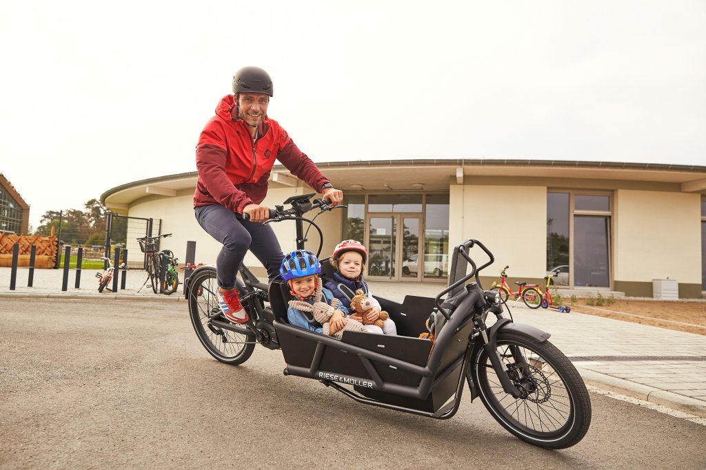 Ein Mann fährt ein Lastenrad mit zwei Kindern.