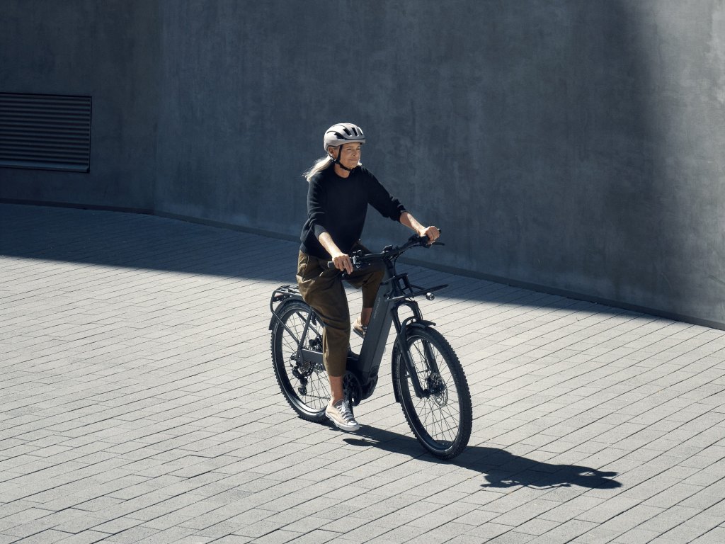 Frau fährt mit E-Bike auf Pflasterweg vor Betonwand.