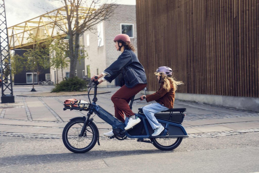 Eine Frau fährt ein E-Lastenrad mit einem Kind auf der hinteren Sitzbank.