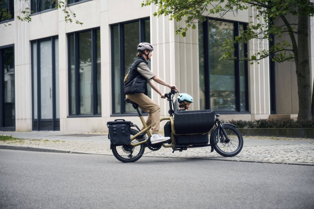 Auf diesem Foto fährt ein junger Mann mit einem Kind in der Transportfläche des Lastenrads „Carrie“.