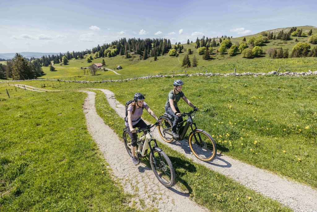 Zwei Frauen fahren einen Weg auf einer Bergwiese entlang.