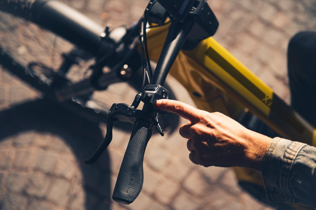Hand zeigt auf Schalter am Lenker eines E-Bikes.