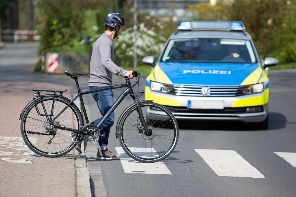 Eine Person schiebt ein Fahrrad über einen Fußgängerüberweg und schaut zu einem Polizeiauto auf der Fahrbahn.
