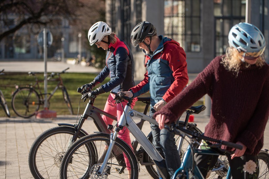 Drei Personen stehen mit E-Bikes auf einem Platz und schauen auf die Bedienelemente am Lenker.