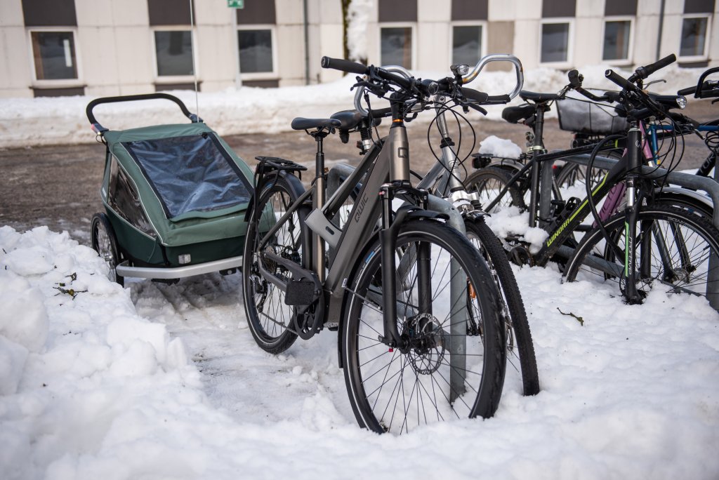 Ein Fahrrad mit Anhänger an einem Abstellbügel. Im Bereich der Stellfläche liegt weniger Schnee als daneben.