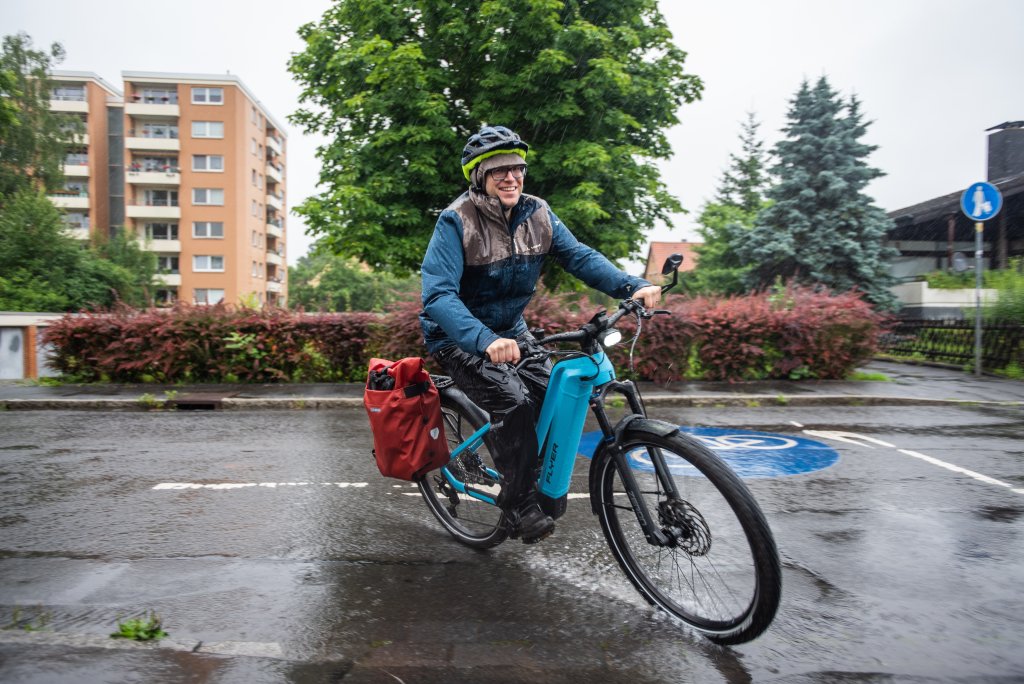 Ein Mann fährt bei Regen auf einem E-Bike durch ein Wohngebiet.