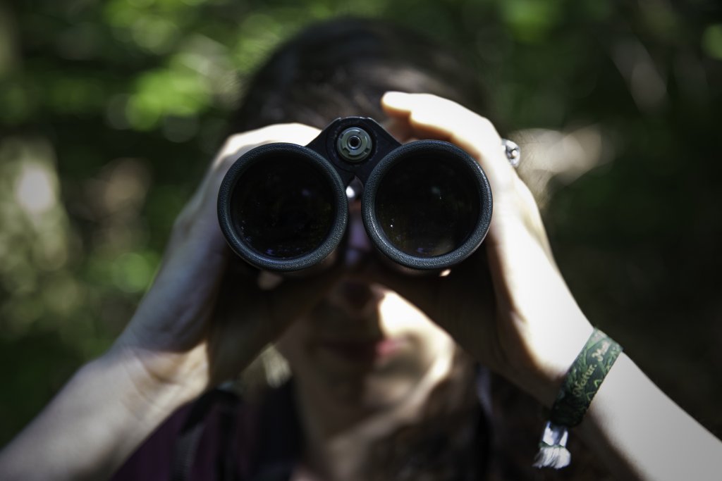 Eine Person schaut durch ein Fernglas in Richtung des Betrachtenden.
