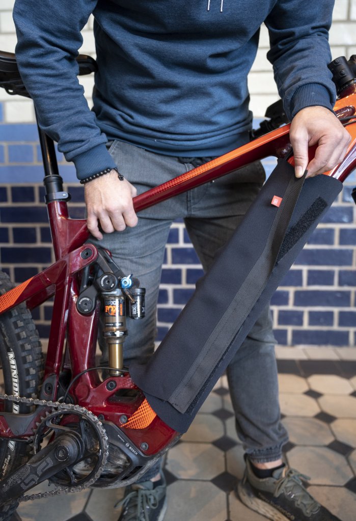 Eine Person wickelt eine Schutzhülle mit Klettverschluss um das Unterrohr und damit den Akku eines E-Bikes.