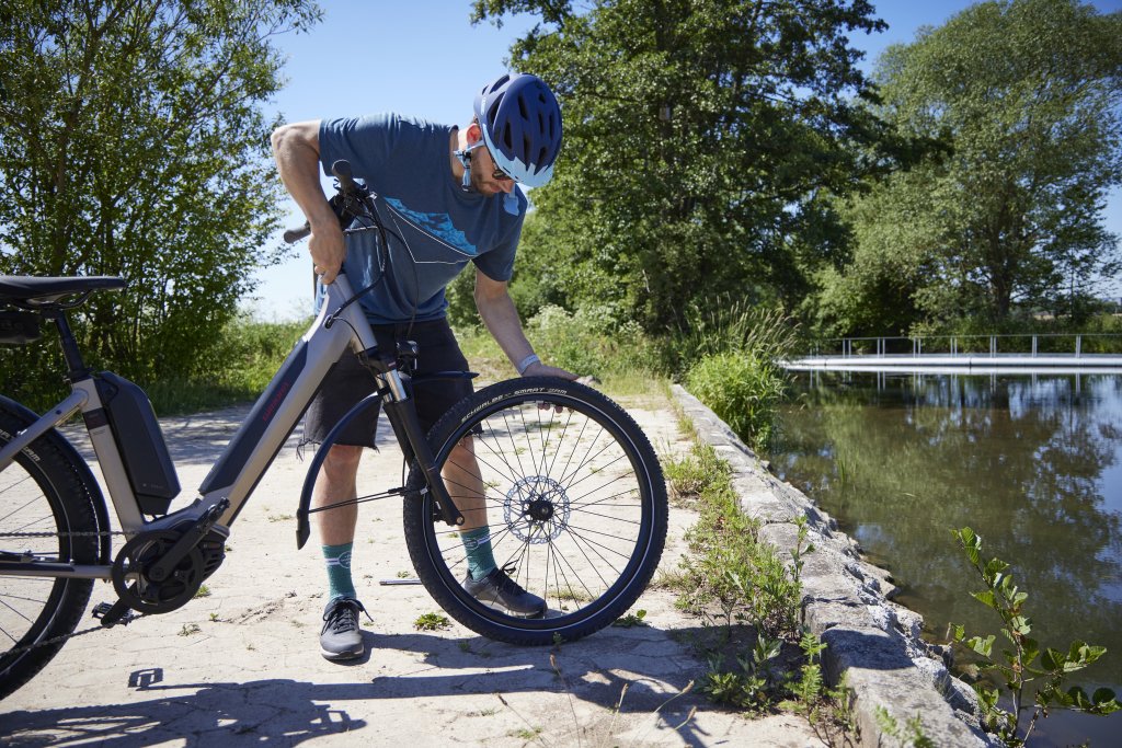 Ein Radfahrer demontiert das Vorderrad aus einem E-Bike am Ufer eines Gewässers.
