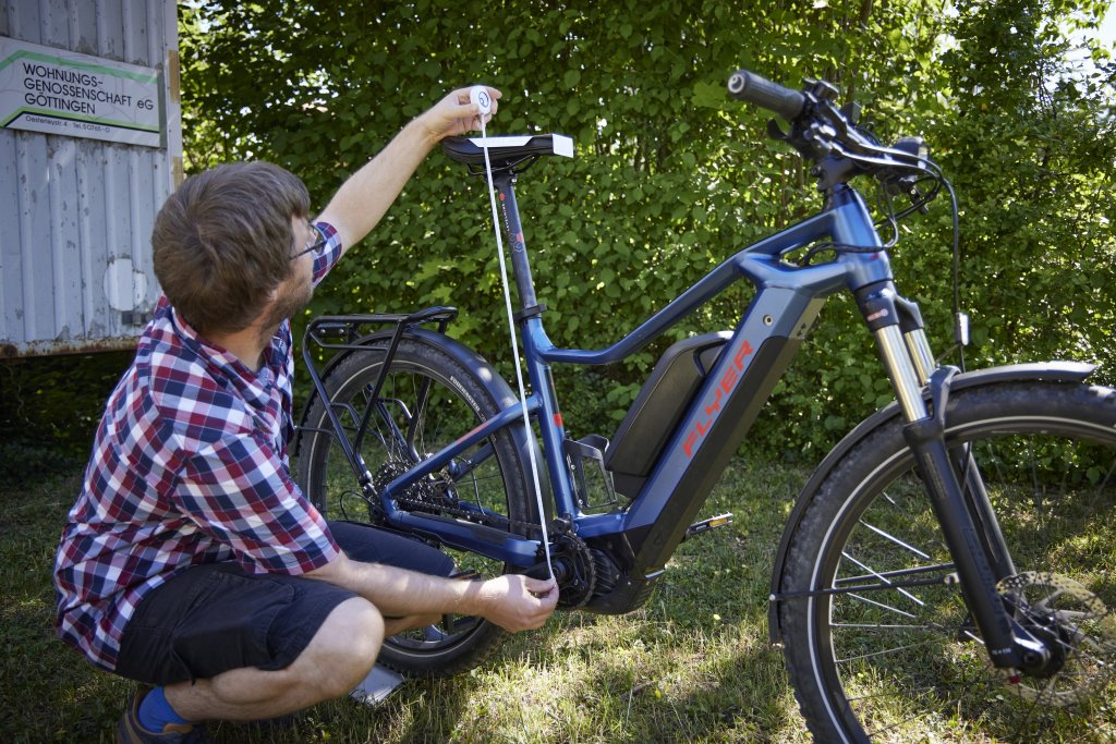 Ein Mann misst an einem E-Bike mit einem Maßband den Abstand zwischen Sattel und Tretlager.