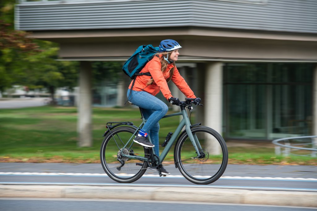 Eine Frau mit einem Rucksack fährt auf einem Fahrrad auf einem Radweg in der Stadt.