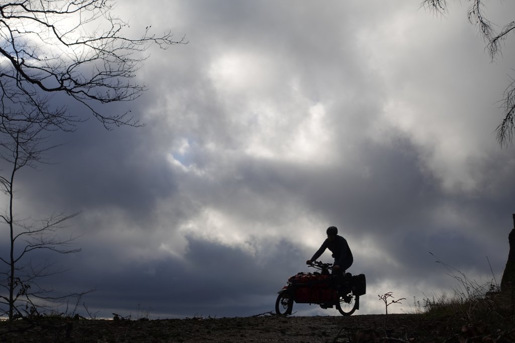 Die Silhouette einer Person auf einem Lastenrad auf dem Horizont vor dunklen Wolken.