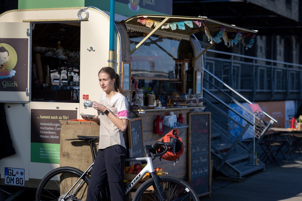 Frau steht mit Tasse Kaffee vor Kiosk