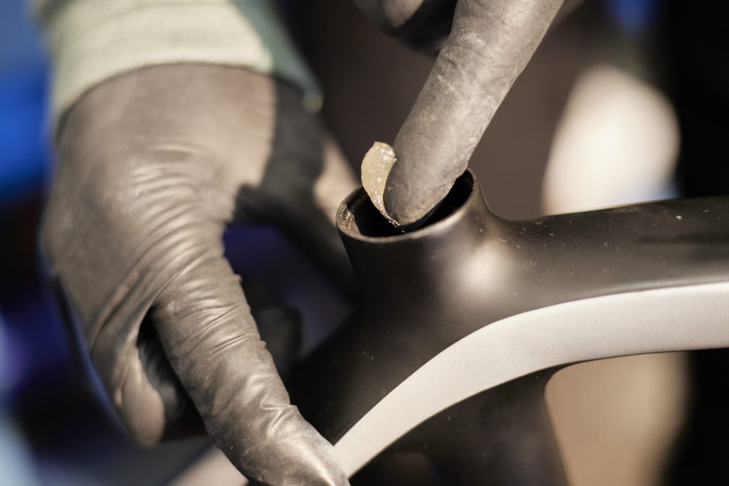 Detailaufnahme des Teils eines Fahrrades, wo die Sattelstütze eingesteckt wird. Eine Person trägt innen mit dem Finger eine helle Paste auf.