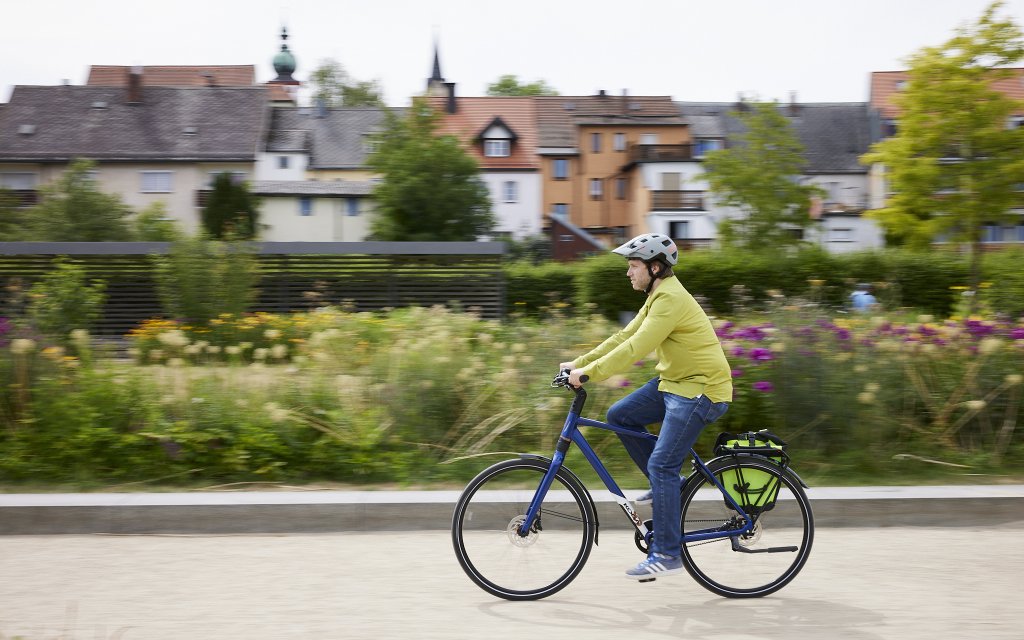 Mann fährt mit Fahrrad vor Blumen.