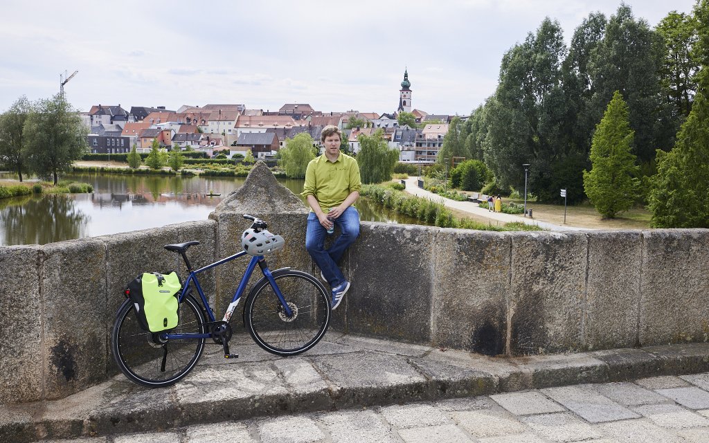 Mann sitzt auf Brücke mit Fahrrad.