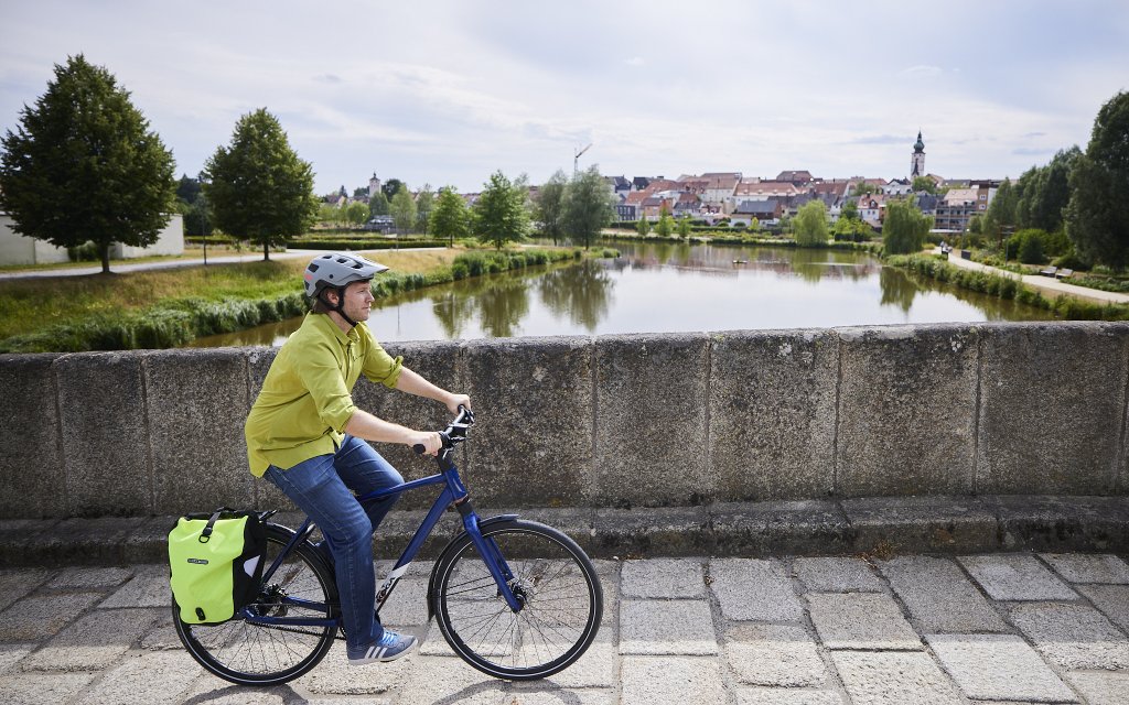 Mann fährt mit Fahrrad über historische Brücke.