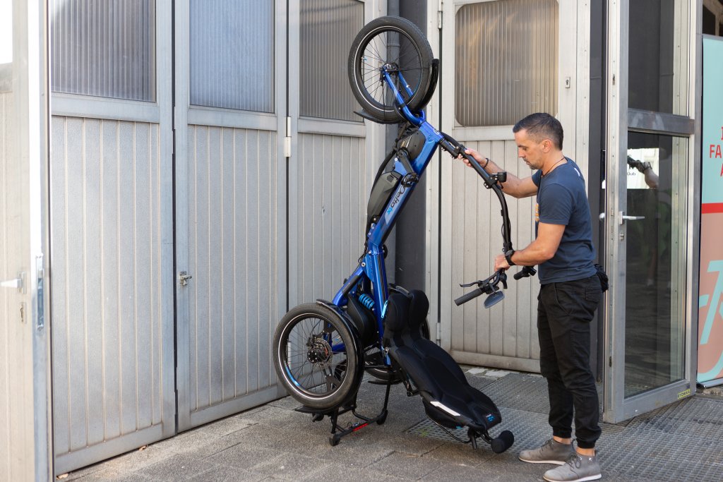 Ein Mann parkt das Sesselrad \\\"Delta tx\\\" von HP Velotechnik aufrecht an einer Wand.