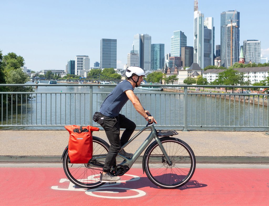 Mann fährt mit pedelec über eine Brücke. Im Hintergrund die Skyline von Frankfurt.