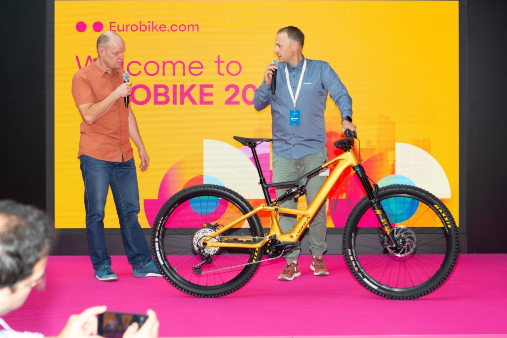 Zwei Männer stehen auf einer Bühne auf der Eurobike mit einem E-MTB.