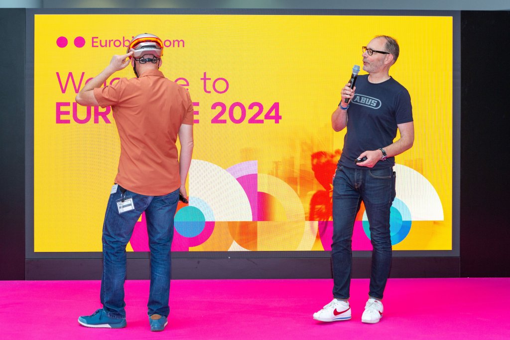 Zwei Männer präsentieren auf einer Bühne auf der Eurobike einen Fahrradhelm.